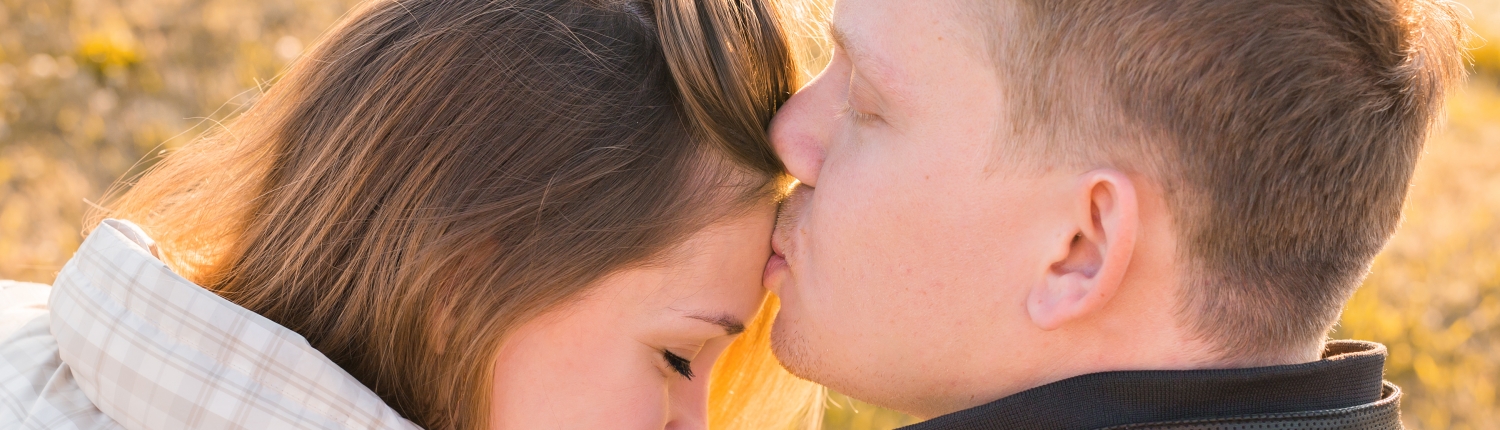Sweet kiss. Handsome young man kissing his girlfriend on forehead in autumn park